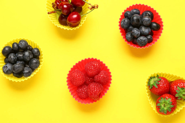 Cupcake molds with different fresh berries on yellow background - Photo, Image