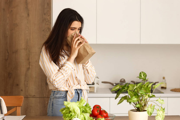 Молодая женщина с бумажным пакетом паникует на кухне - Фото, изображение