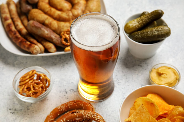 Szklanka zimnego piwa i różne przekąski na jasnym tle. Święto Oktoberfest - Zdjęcie, obraz