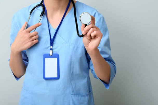 Жінка-лікар зі стетоскопом і значком на сірому фоні - Фото, зображення