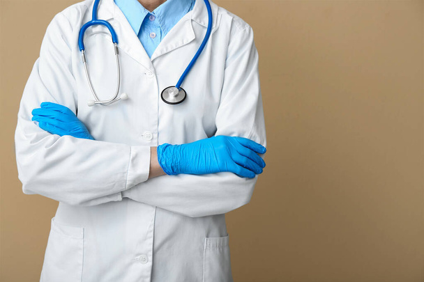 Vrouwelijke arts met stethoscoop en medische handschoenen op beige achtergrond - Foto, afbeelding