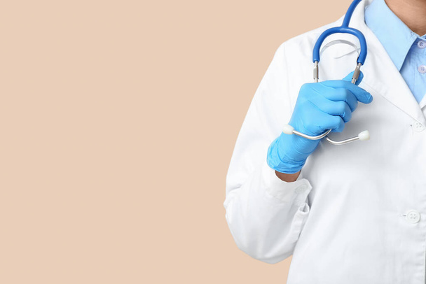 Female doctor with stethoscope and medical gloves on beige background - Valokuva, kuva