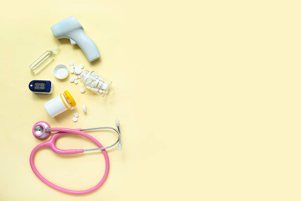 Stethoskop, Pillen, Pulsoximeter, Infrarot-Thermometer und Ampulle auf gelbem Hintergrund - Foto, Bild