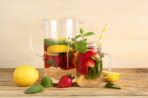 Mason jar and jug of fresh lemonade with strawberry on wooden table - Fotó, kép