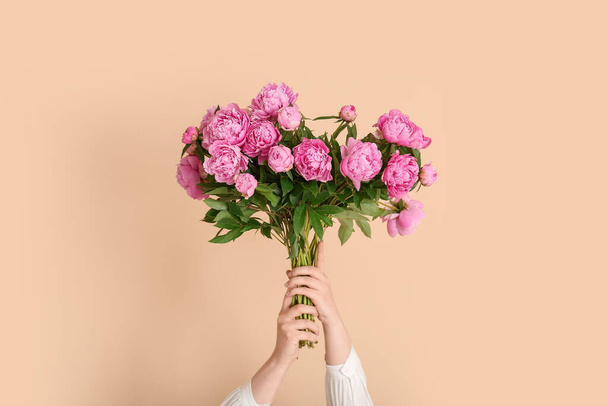 Mani femminili con bouquet di peonie rosa su sfondo beige - Foto, immagini