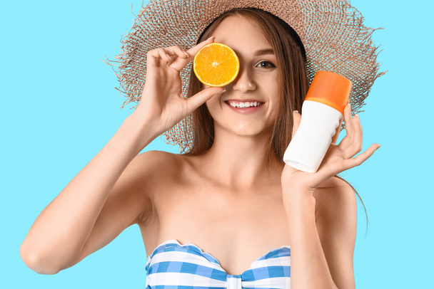 Young woman with sunscreen cream and orange on blue background, closeup - Фото, зображення