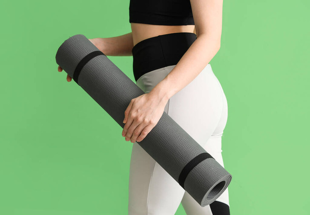 Jonge vrouw in sportkleding en met yoga mat op groene achtergrond - Foto, afbeelding