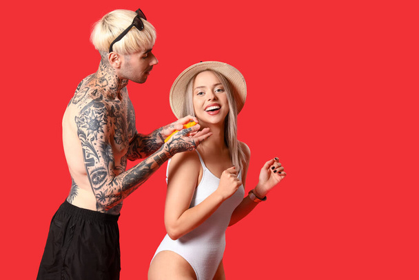 Young couple with sunscreen cream on red background - Foto, afbeelding