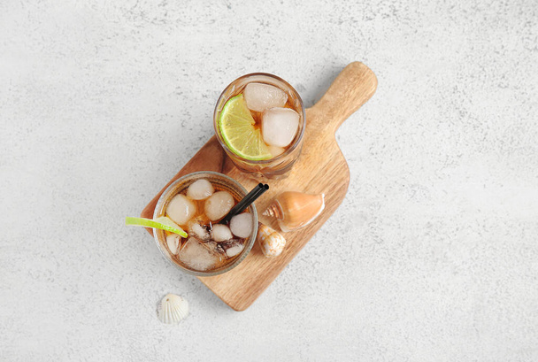 Board with glasses of cold Cuba Libre cocktail and seashells on white background - 写真・画像