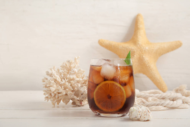 Glass of cold Cuba Libre cocktail, coral, seashell and starfish on white wooden table - Фото, зображення