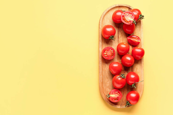 Deska drewniana ze świeżymi pomidorami wiśniowymi na żółtym tle - Zdjęcie, obraz