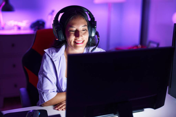 Νεαρή όμορφη ισπανόφωνη γυναίκα streamer παίζει βιντεοπαιχνίδι χρησιμοποιώντας υπολογιστή στην αίθουσα τυχερών παιχνιδιών - Φωτογραφία, εικόνα