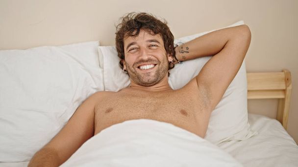 Fiatal spanyol férfi pihent az ágyon mosolyogva félmeztelenül a hálószobában - Fotó, kép