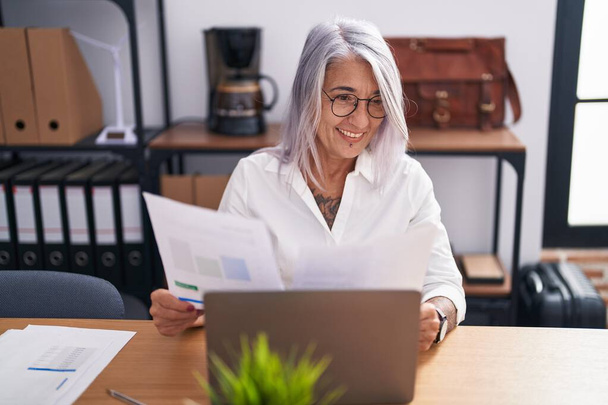 Жінка середнього віку сіроока бізнесмен використовує документ для читання ноутбуків в офісі
 - Фото, зображення