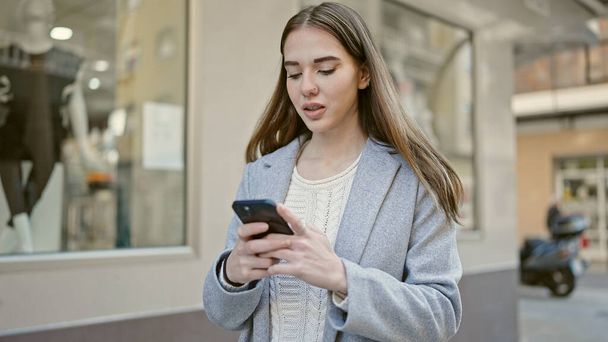 Молода іспаномовна жінка використовує смартфон, який виглядає засмученим на вулиці
 - Фото, зображення