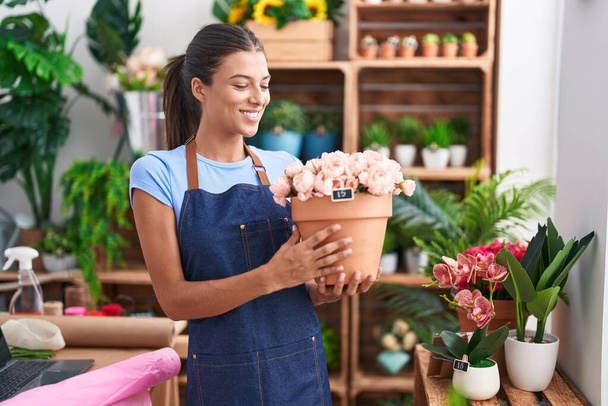 Jovem bela mulher hispânica florista sorrindo confiante segurando planta na florista - Foto, Imagem