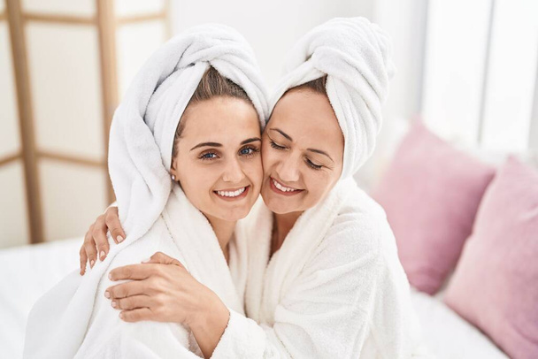 Two women mother and daughter wearing bathrobe hugging each other at bedroom - Φωτογραφία, εικόνα