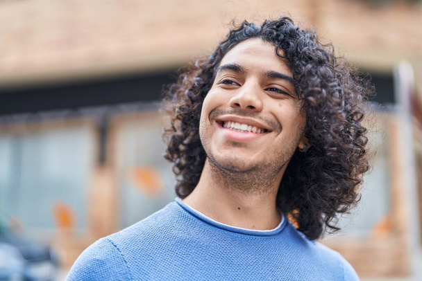 Молодий латинський чоловік посміхається впевнено дивлячись в сторону на вулиці
 - Фото, зображення