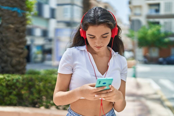 Young hispanic woman listening to music at park - 写真・画像