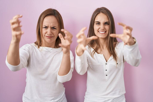 Middle age mother and young daughter standing over pink background shouting frustrated with rage, hands trying to strangle, yelling mad  - Photo, Image