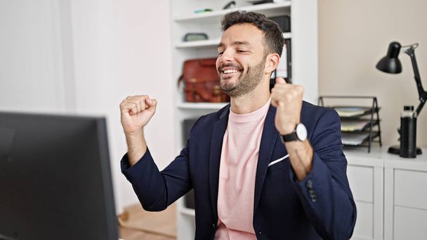 Nuori latino mies liiketoiminnan työntekijä käyttää tietokonetta voittaja ele toimistossa - Valokuva, kuva