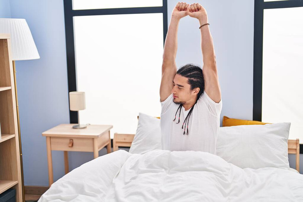 Νεαρός άντρας απλώνει τα χέρια του στο κρεβάτι στην κρεβατοκάμαρα - Φωτογραφία, εικόνα
