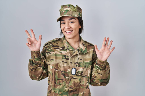 Nuori eteläaasialainen nainen yllään naamiointi armeijan univormu näyttää ja osoittaa sormilla numero kahdeksan hymyillen itsevarma ja onnellinen.  - Valokuva, kuva