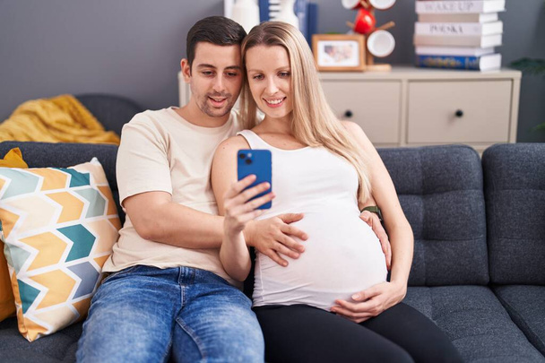 Mies ja nainen pari koskettaa vatsaa älypuhelimella kotona - Valokuva, kuva