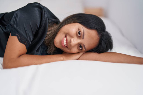Молода іспаномовна жінка посміхається впевнено лежить на ліжку в спальні
 - Фото, зображення