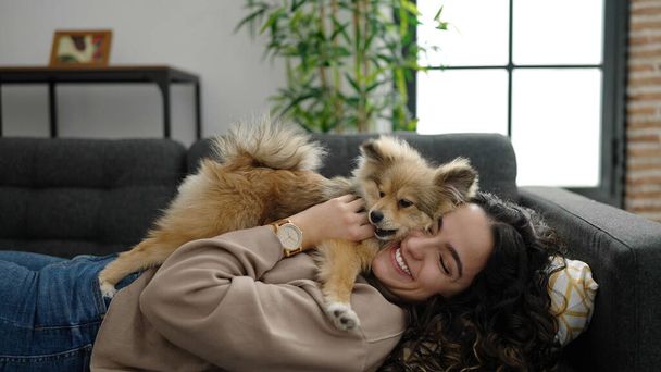 Mujer hispana joven con perro acostado en el sofá jugando en casa - Foto, imagen