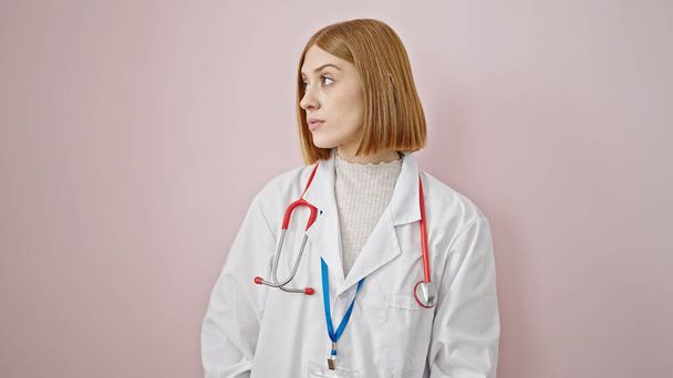 Jeune femme blonde médecin debout avec une expression sérieuse sur fond rose isolé - Photo, image