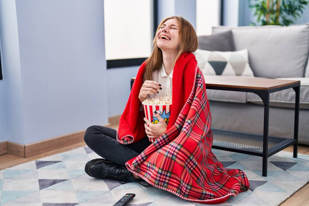 Young blonde woman watching movie sitting on floor at home - Photo, image