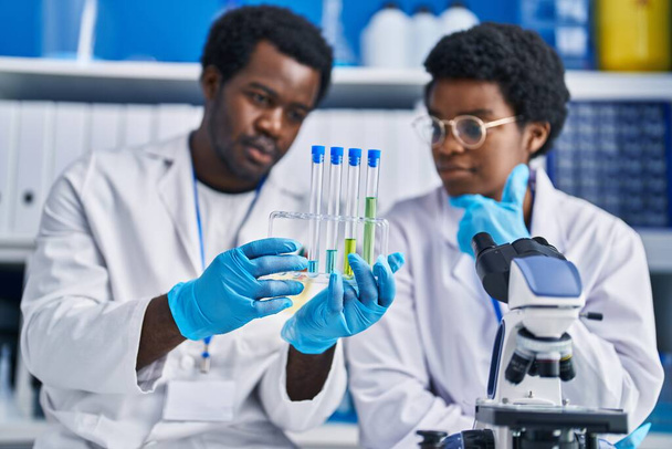 アフリカ系アメリカ人の男性と女性科学者が実験室で試験管を持っている - 写真・画像