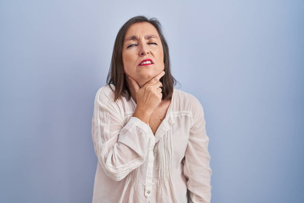 Middle age hispanic woman standing over blue background touching painful neck, sore throat for flu, clod and infection  - Photo, Image