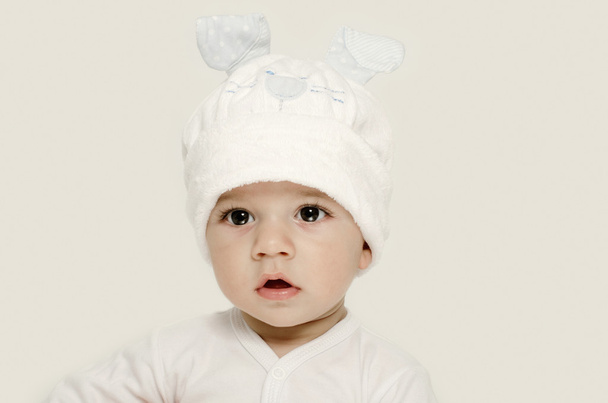 Innocent baby wearing a white hat looking adorable. Kid dressed for winter, lovely newborn. Adorable baby portrait looking curious. Baby dressed as a funny bunny with a white hat with rabbit ears - Fotó, kép