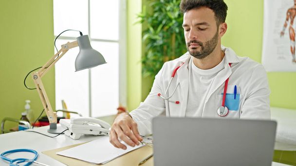 Joven médico hispano usando laptop trabajando en clínica - Foto, imagen