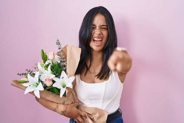 Μπρουνέτ γυναίκα κρατώντας μπουκέτο από λευκά λουλούδια δείχνοντας δυσαρεστημένος και απογοητευμένος από την κάμερα, θυμωμένος και έξαλλος μαζί σας  - Φωτογραφία, εικόνα