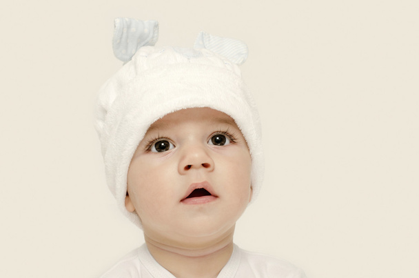 罪のない赤ちゃん見て愛らしい白い帽子をかぶっています。子供は、冬、素敵な新生児の服を着てください。愛らしい赤ちゃんの肖像画見て好奇心。白い帽子のウサギの耳おかしいバニーに扮した赤ちゃん - 写真・画像