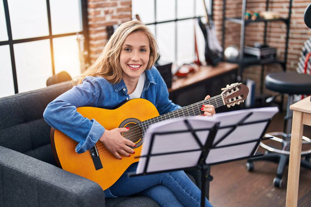 Νεαρή ξανθιά γυναίκα μουσικός παίζει κλασική κιθάρα στο στούντιο μουσικής - Φωτογραφία, εικόνα
