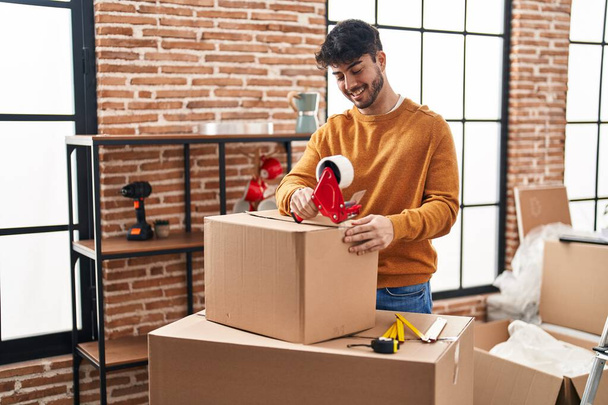 Young hispanic man smiling confident packing cardboard box at new home - Foto, Imagen