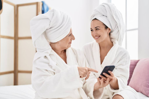 Mother and daughter wearing bathrobe using smartphone at bedroom - Foto, Bild