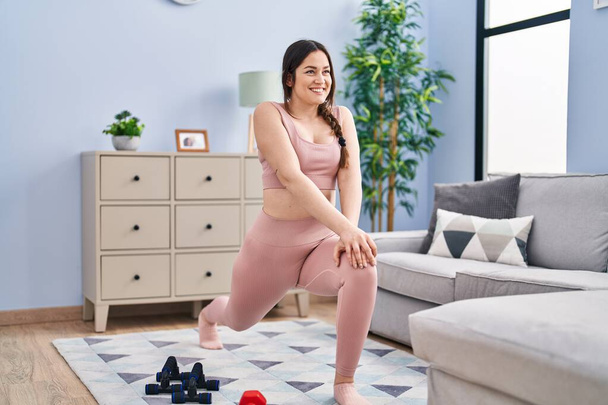 Mujer joven sonriendo confiado entrenamiento piernas ejercicio en casa - Foto, Imagen