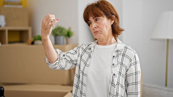 Mujer de mediana edad buscando llaves de la casa con expresión triste en el nuevo hogar - Foto, Imagen