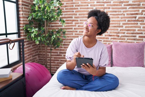 donna afroamericana utilizzando touchpad seduto sul letto in camera da letto - Foto, immagini