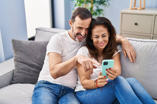 Střední věk muž a žena pár pomocí smartphone sedí na pohovce doma - Fotografie, Obrázek