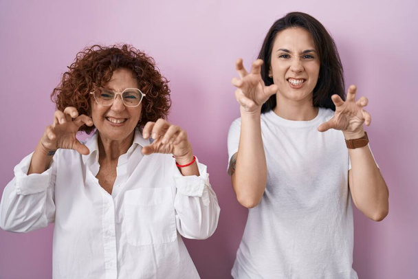 Mère et fille hispaniques portant un t-shirt blanc décontracté sur fond rose souriant drôle faisant griffe geste comme chat, expression agressive et sexy  - Photo, image