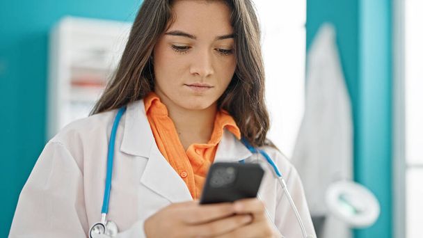 Young beautiful hispanic woman doctor using smartphone at clinic - Фото, зображення