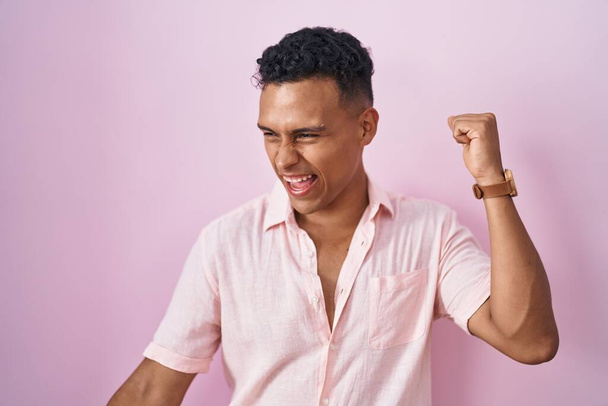 Young hispanic man standing over pink background dancing happy and cheerful, smiling moving casual and confident listening to music  - Zdjęcie, obraz