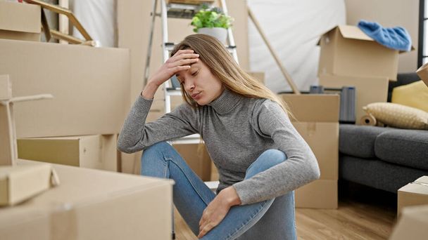 Young caucasian woman sitting on floor with worried expression at new home - Photo, image