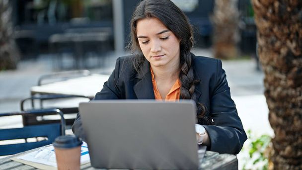 Молода красива іспанська жінка бізнесмен використовує ноутбук з розслабленим виразом на терасі кав'ярні
 - Фото, зображення
